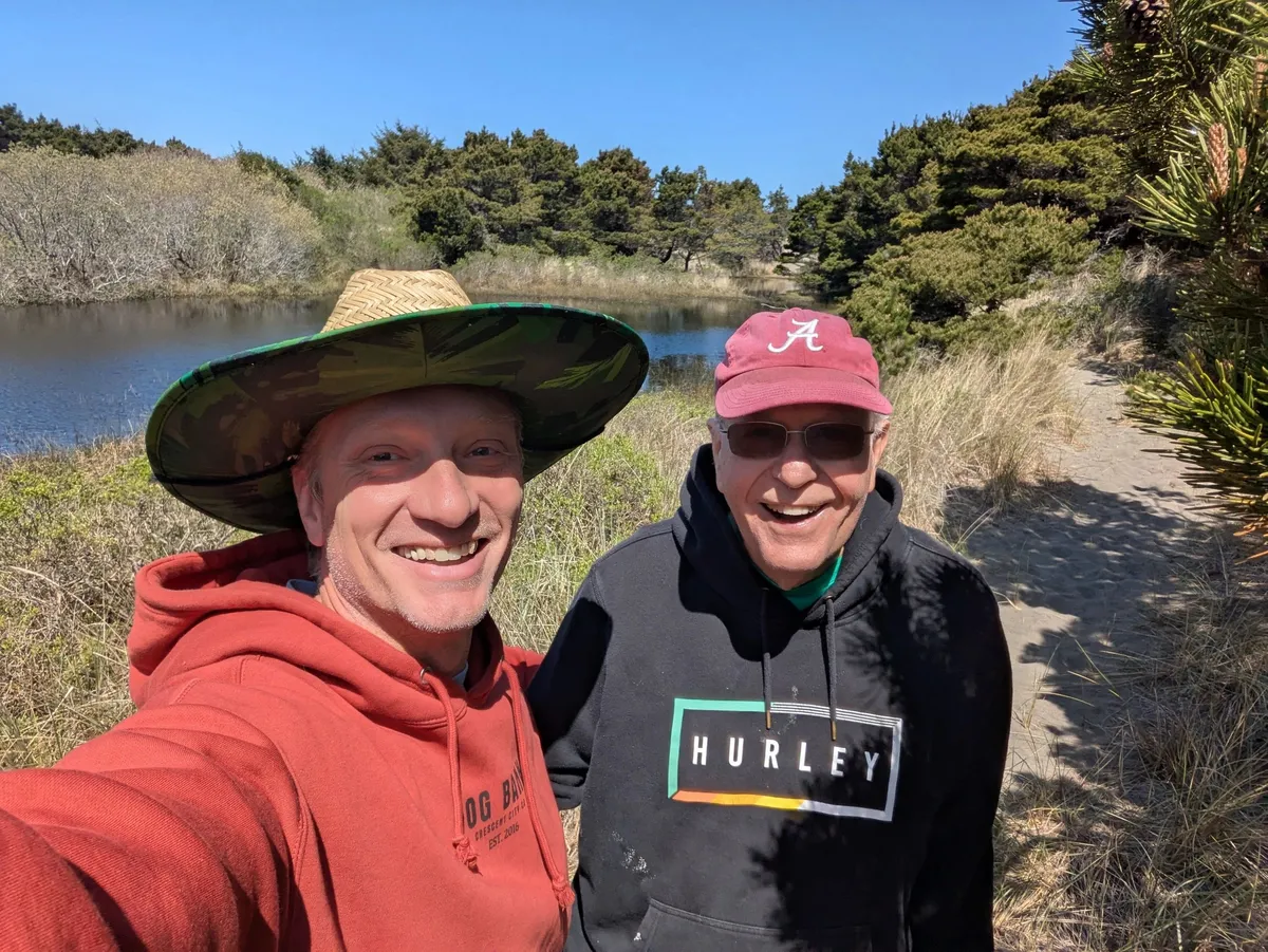Two smiling people beside the water on a sunny day.