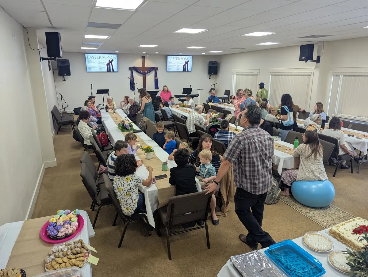 People of different ages sharing a meal at long tables inside the church on Resurrection Sunday 2025.