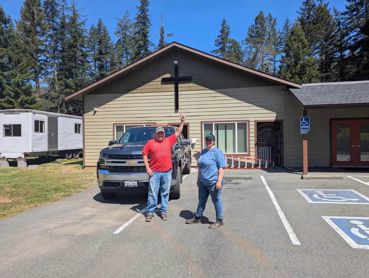 Two people standing by a truck outside the church building.