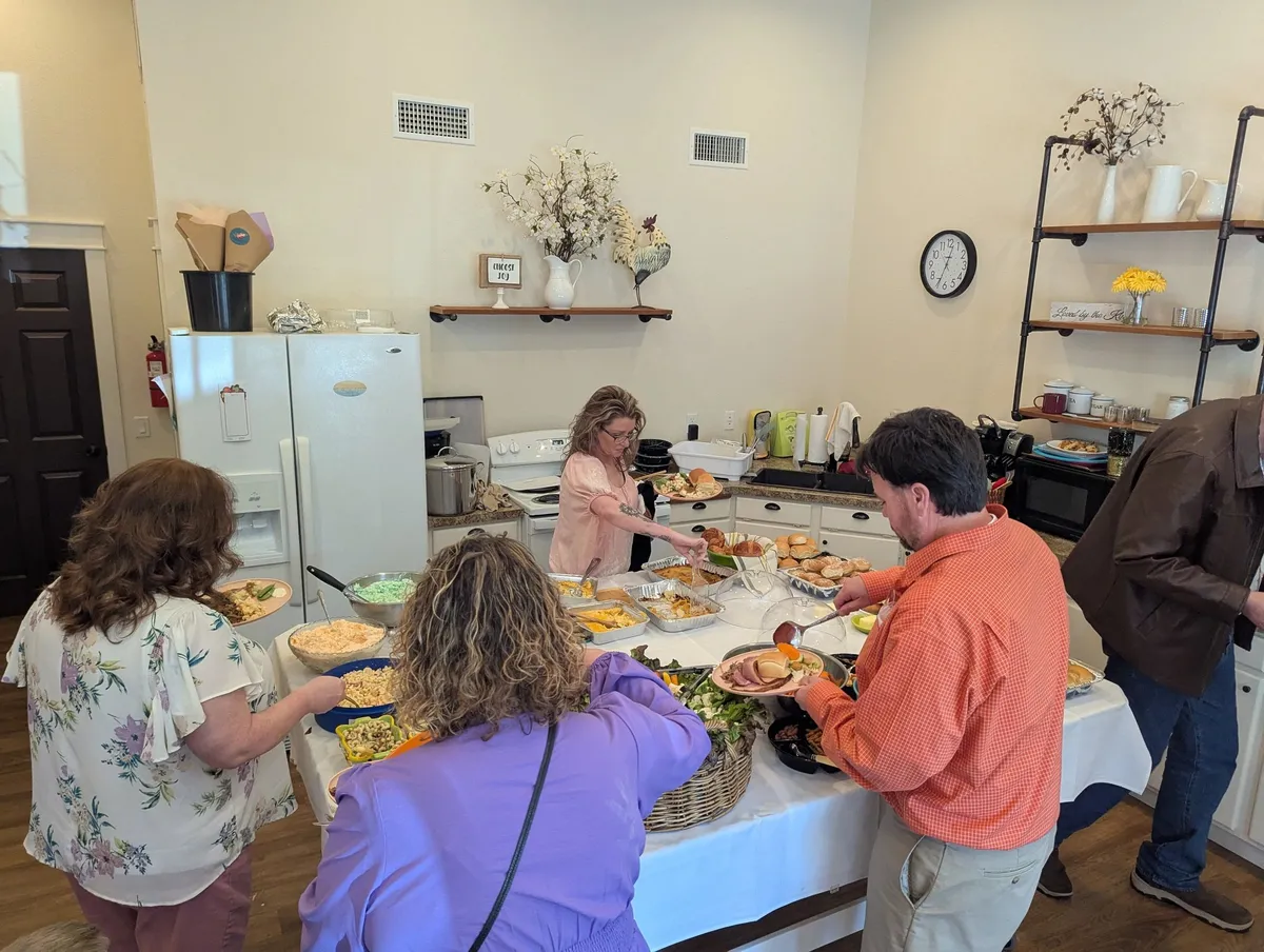 People seated and standing around a table sharing a meal.